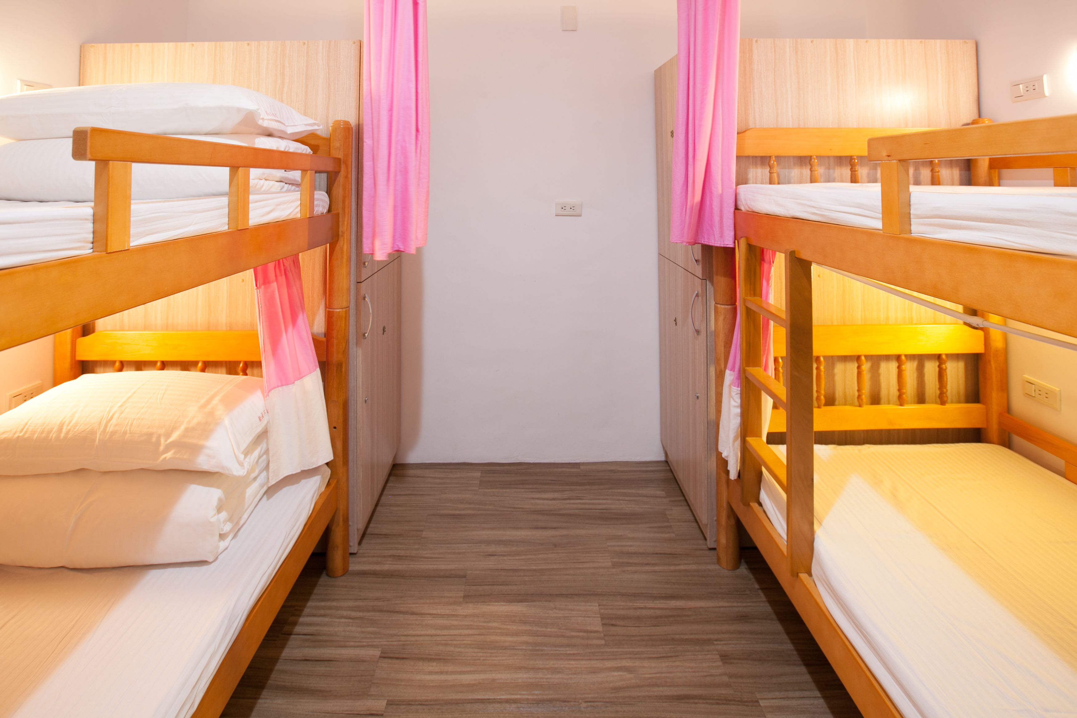 A room with two bunk beds, wooden flooring, and a white wall.