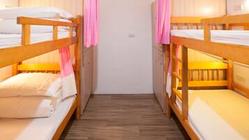 A room with two bunk beds, wooden flooring, and a white wall.
