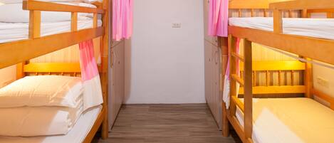 A room with two bunk beds, wooden flooring, and a white wall.