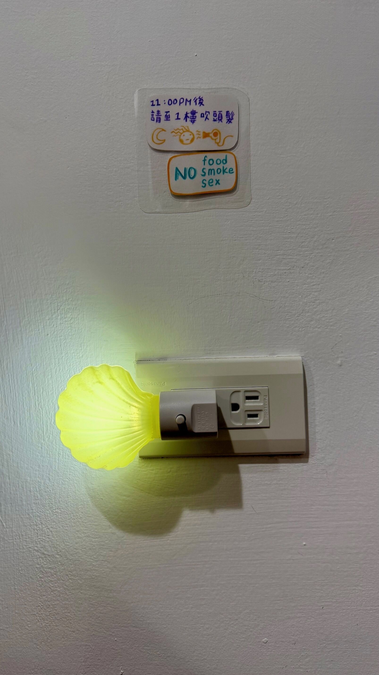 A wall-mounted light fixture with a yellow bulb and a plug.
