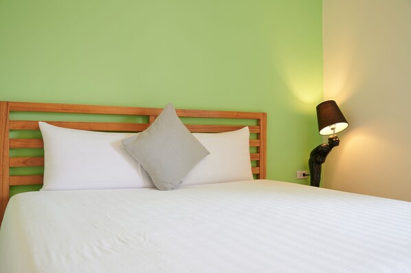 Una cama bien hecha con sábanas blancas y dos almohadas, cabecera de madera y una lámpara fijada a la pared.