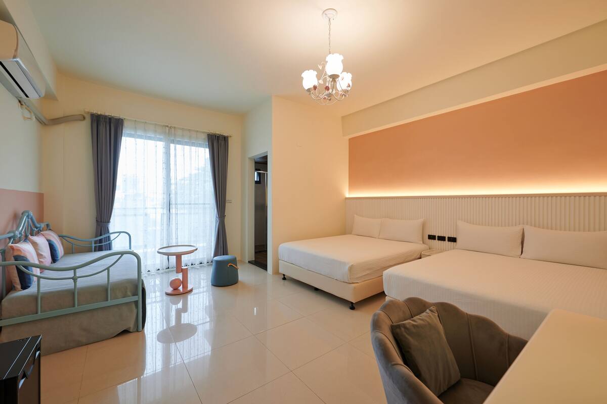 A modern hotel room with a bed, a sofa, a small table, and a chandelier.
