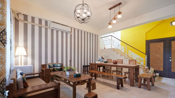 A spacious living area with a wooden dining set, striped wallpaper, and a staircase leading to a bright yellow room. - Avenue B&B (Hualien City)