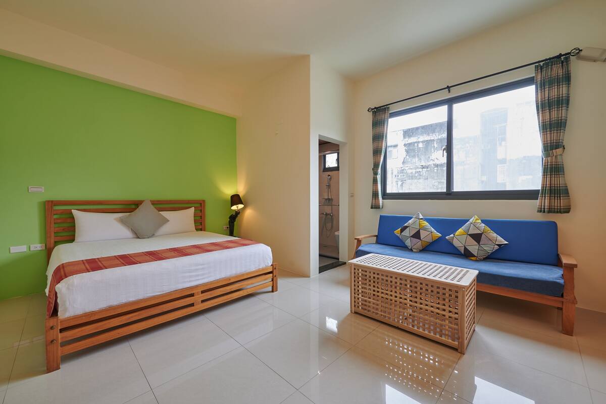 A bedroom with a bed, a wooden bench, a wicker basket, and a window with curtains.