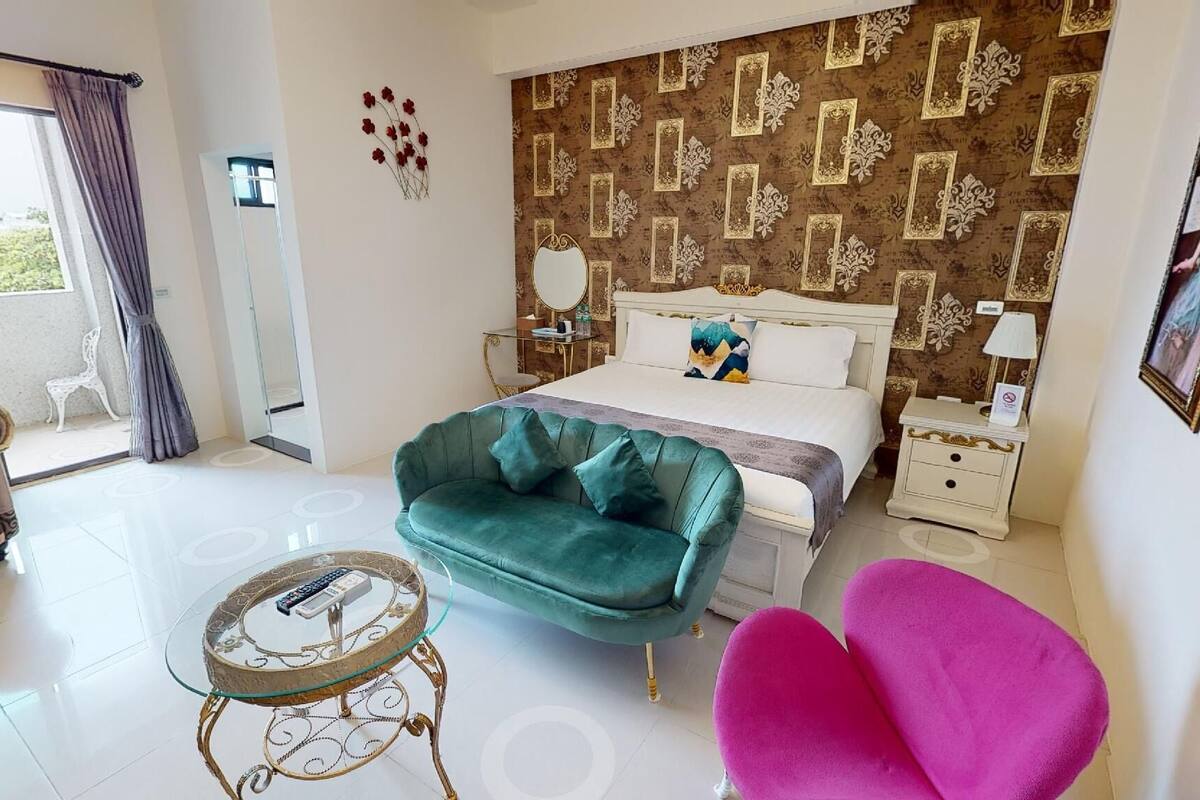 A modern bedroom with a large bed, a green sofa, a pink chair, and a glass coffee table.