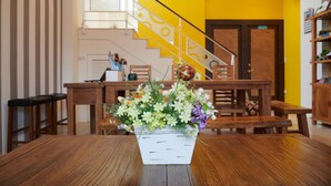 A wooden table with a white vase of flowers in the center, a staircase with yellow walls, and wooden furniture. - Avenue B&B (Hualien City)