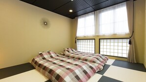 A room with tatami mat flooring, a bed with a checkered bedspread, a skylight, and a window with curtains.