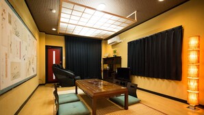A room with a wooden table, green cushioned seating, a ceiling light fixture, a wall-mounted air conditioner, and a decorative wall with framed artwork.