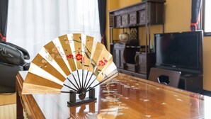 A traditional fan with floral designs on a wooden table in a room with a TV, bookshelf, and curtains.