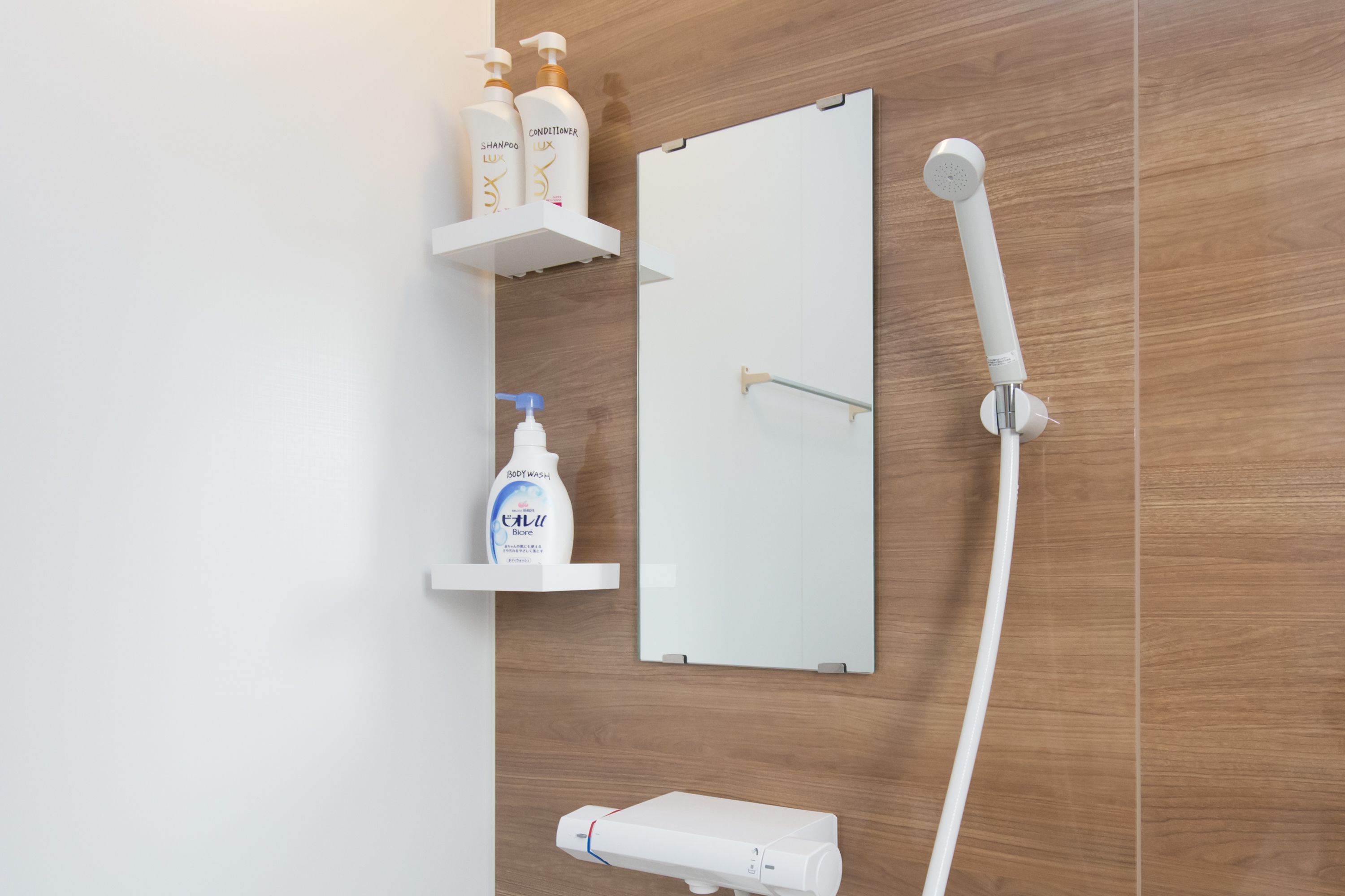A bathroom with a wooden wall, a white shower enclosure, a mirror, and a shelf with toiletries.