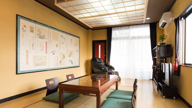 A conference room with a glass-top table, green cushioned chairs, a large framed artwork on the wall, and a black leather sofa.
