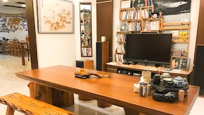 A modern living room with a wooden dining table, benches, a flat-screen TV, bookshelves, and a coffee station. - Greenpark Homestay (Luodong)