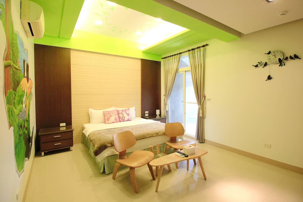 A hotel room with a bed, two chairs, a small table, and a painting on the wall.