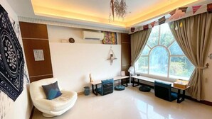 A modern living room with a large window, a white chair, a small table, and a wall-mounted air conditioner. - Greenpark Homestay (Luodong)