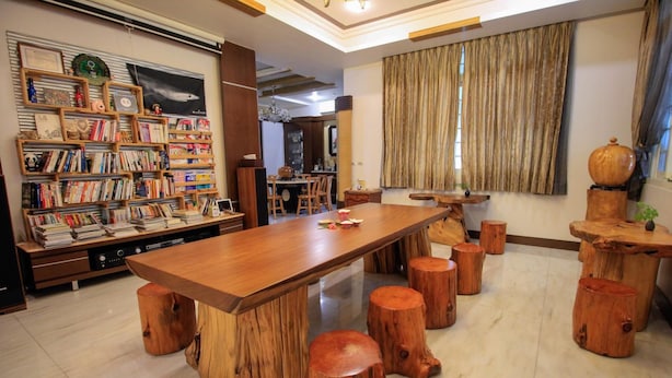 A spacious room with a long wooden table surrounded by stools, a bookshelf filled with books, and a large window with curtains. - Greenpark Homestay (Luodong)