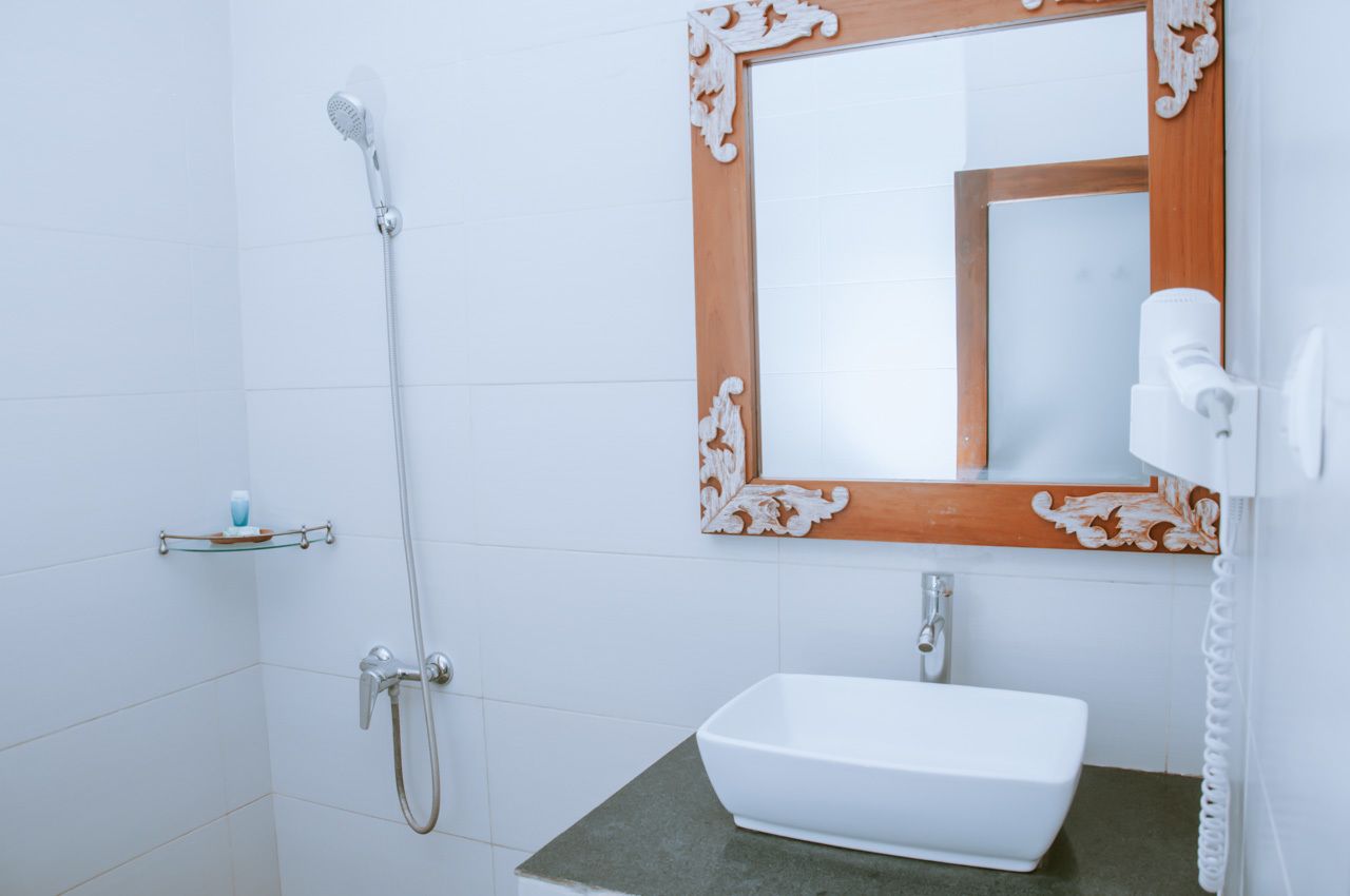 A bathroom with a white sink, a mirror with a wooden frame, and a shower with a handheld showerhead.