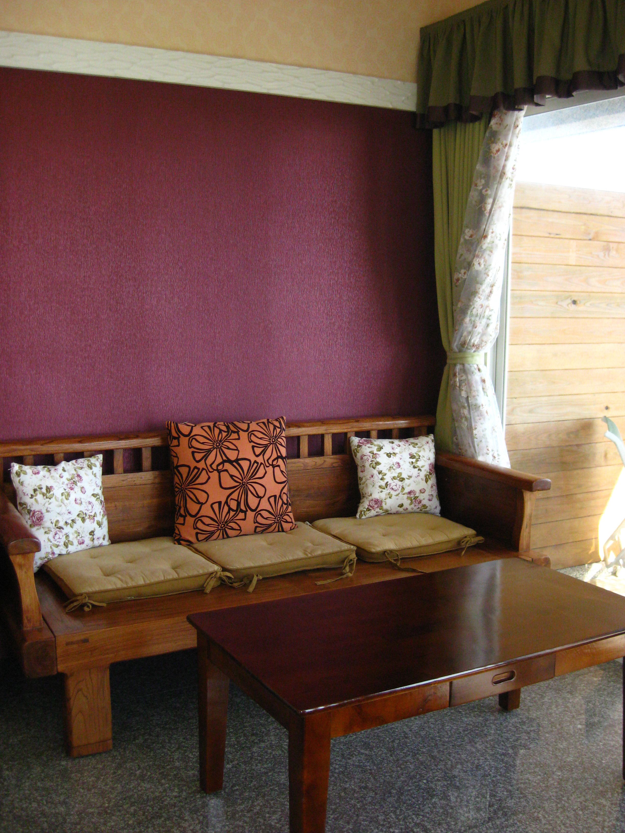 A wooden bench with cushioned seats and floral-patterned pillows, a wooden table in front, and a window with curtains.