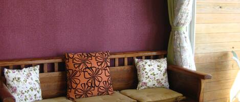 A wooden bench with cushioned seats and floral-patterned pillows, a wooden table in front, and a window with curtains.