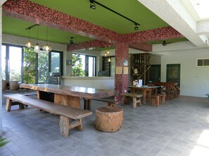 Un amplio espacio exterior con mesas y bancos de madera, techo verde y vistas a árboles.