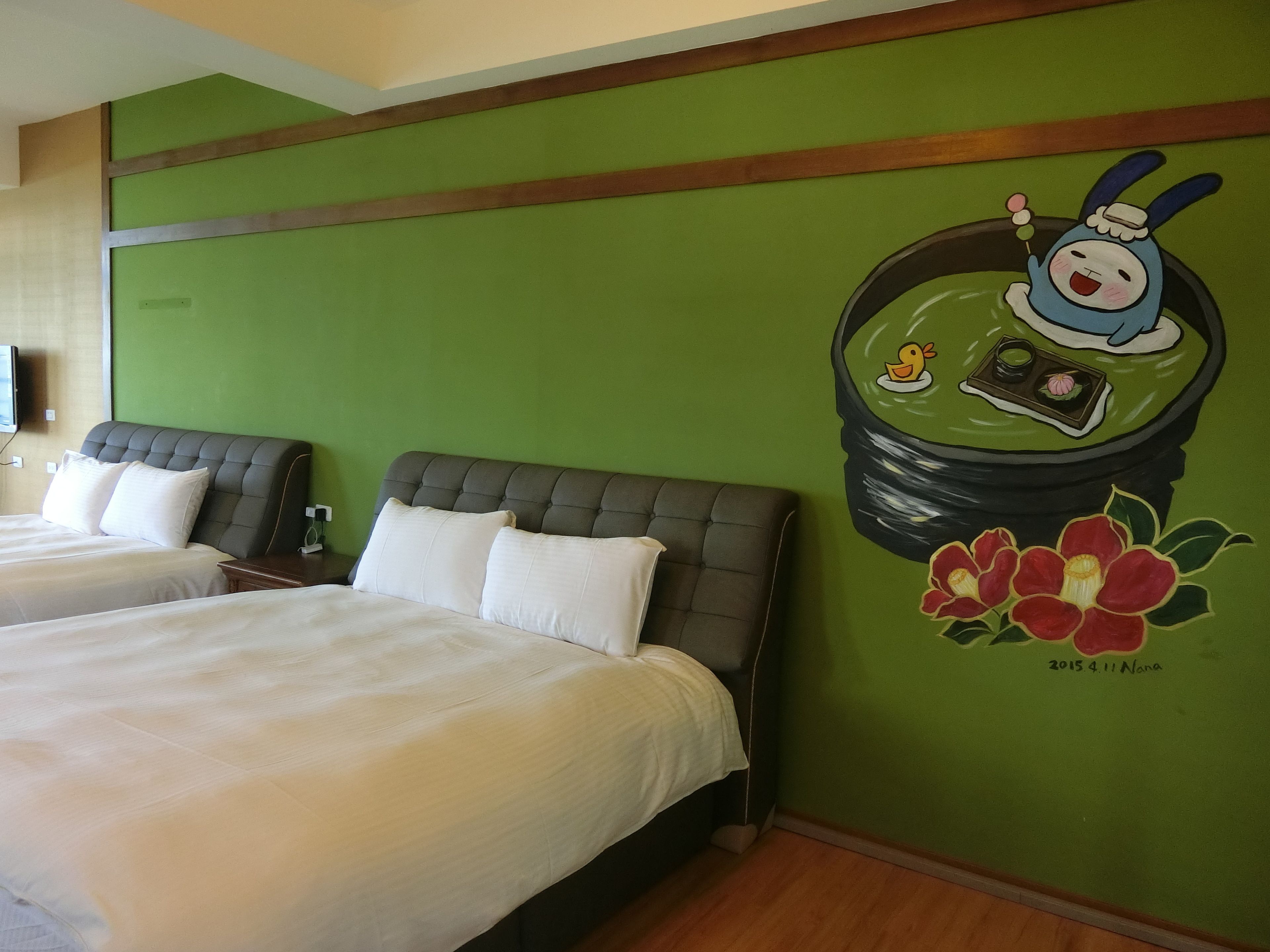 A hotel room with two beds, green walls, and a mural of a cartoon character.