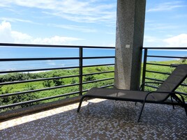 A balcony with a view of the ocean, a tree, and a tiled floor.