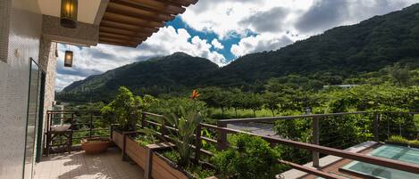 Un balcón con vistas a un paisaje montañoso, barandas de madera y plantas en macetas.