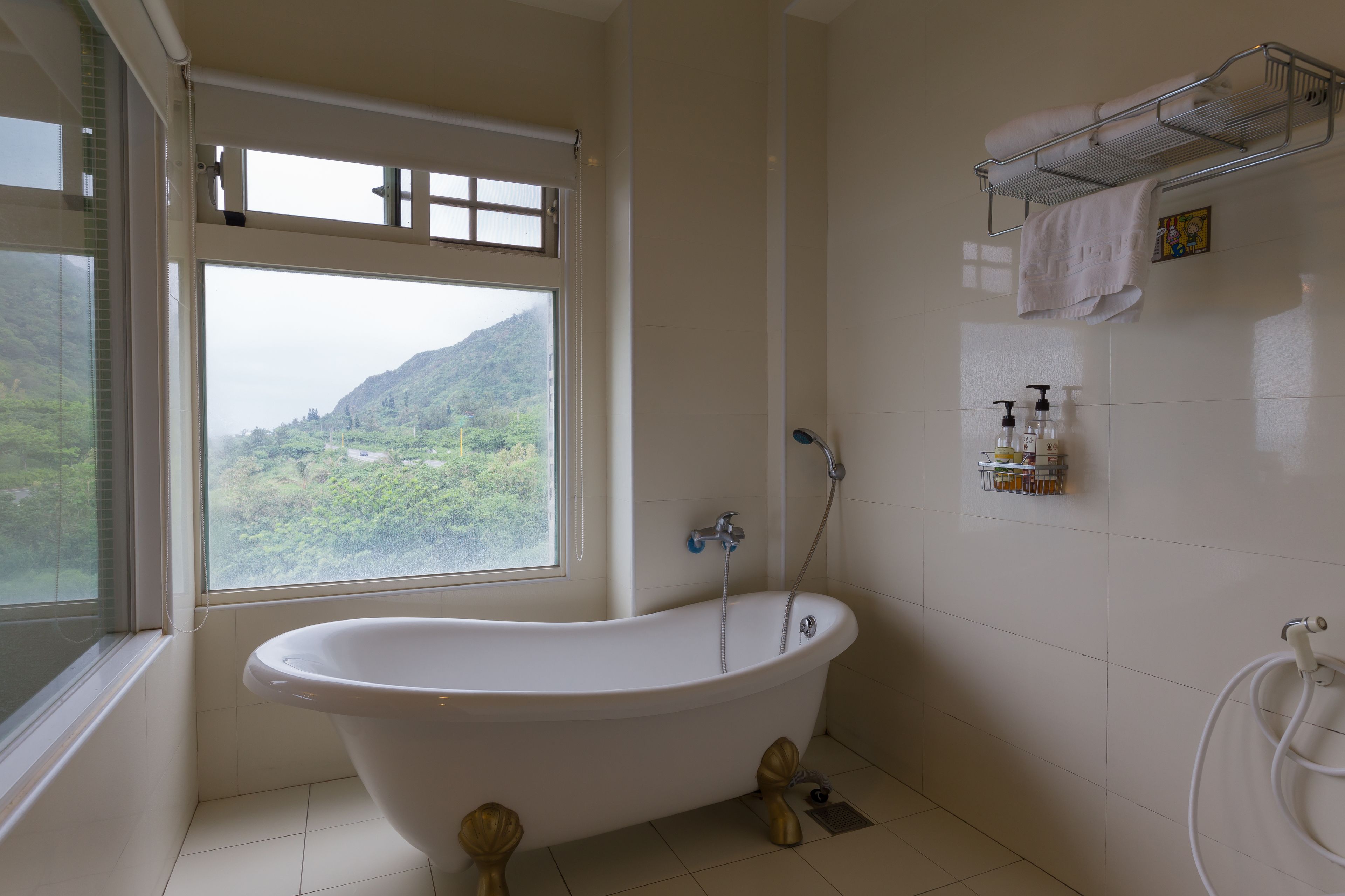 A bathroom with a freestanding bathtub, a window with a view of greenery, and a towel rack with towels.