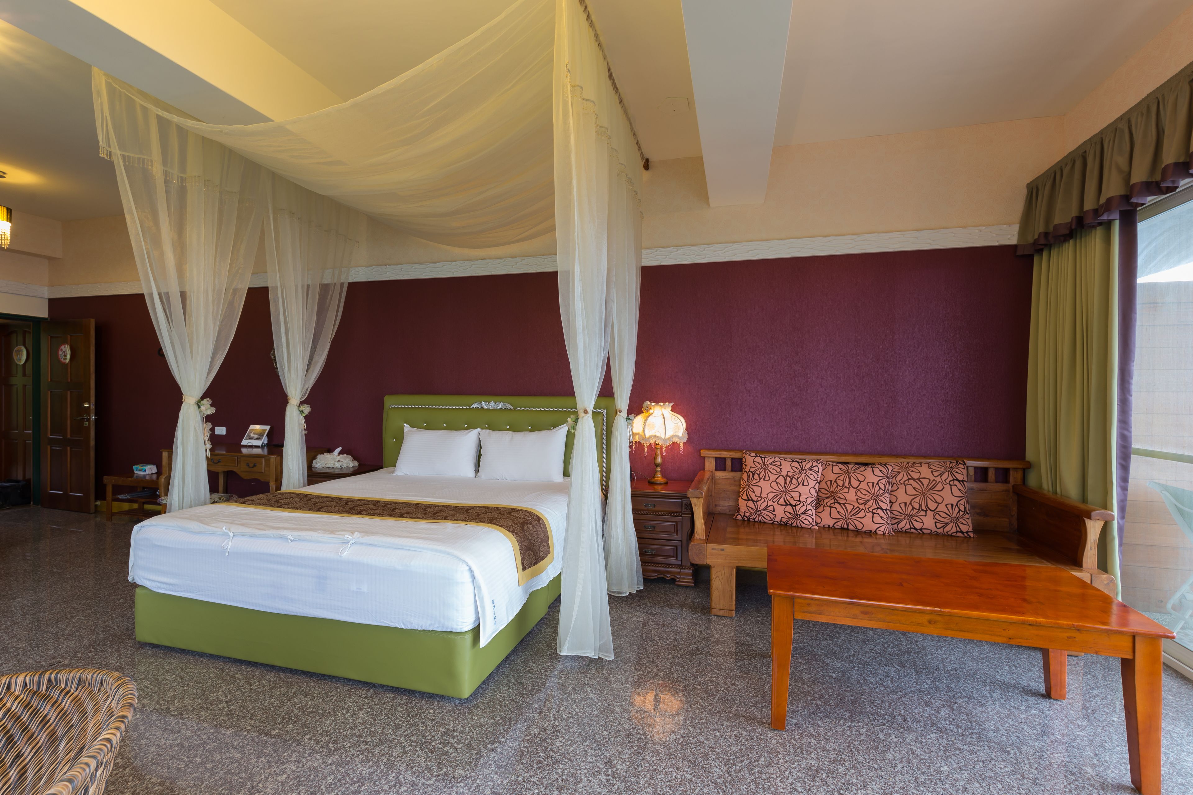 A room with a bed, a wooden table, a bench, and a nightstand with a lamp.