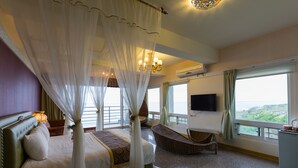 Un dormitorio con cama con dosel, televisor de pantalla plana, un ventanal con vistas y una mesita de noche con lámpara.