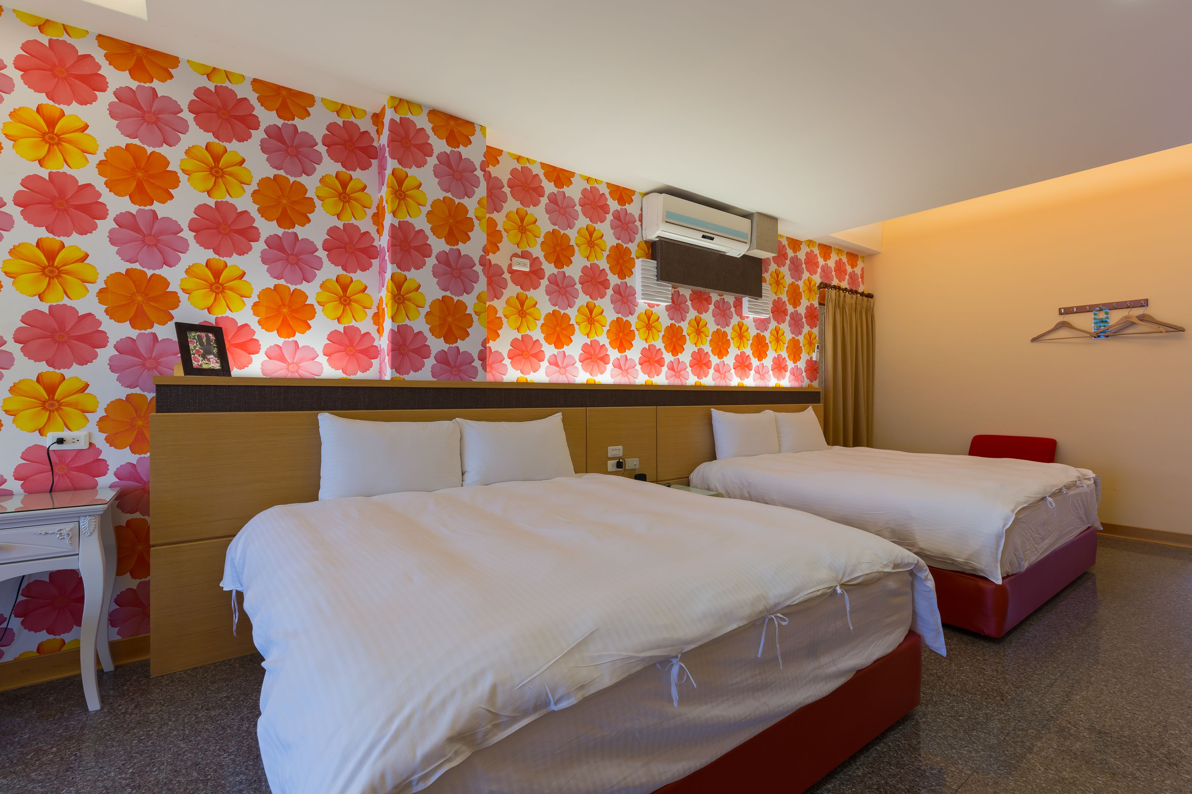 Une chambre d’hôtel avec deux lits, un petit bureau, une armoire et un papier peint à motifs floraux.