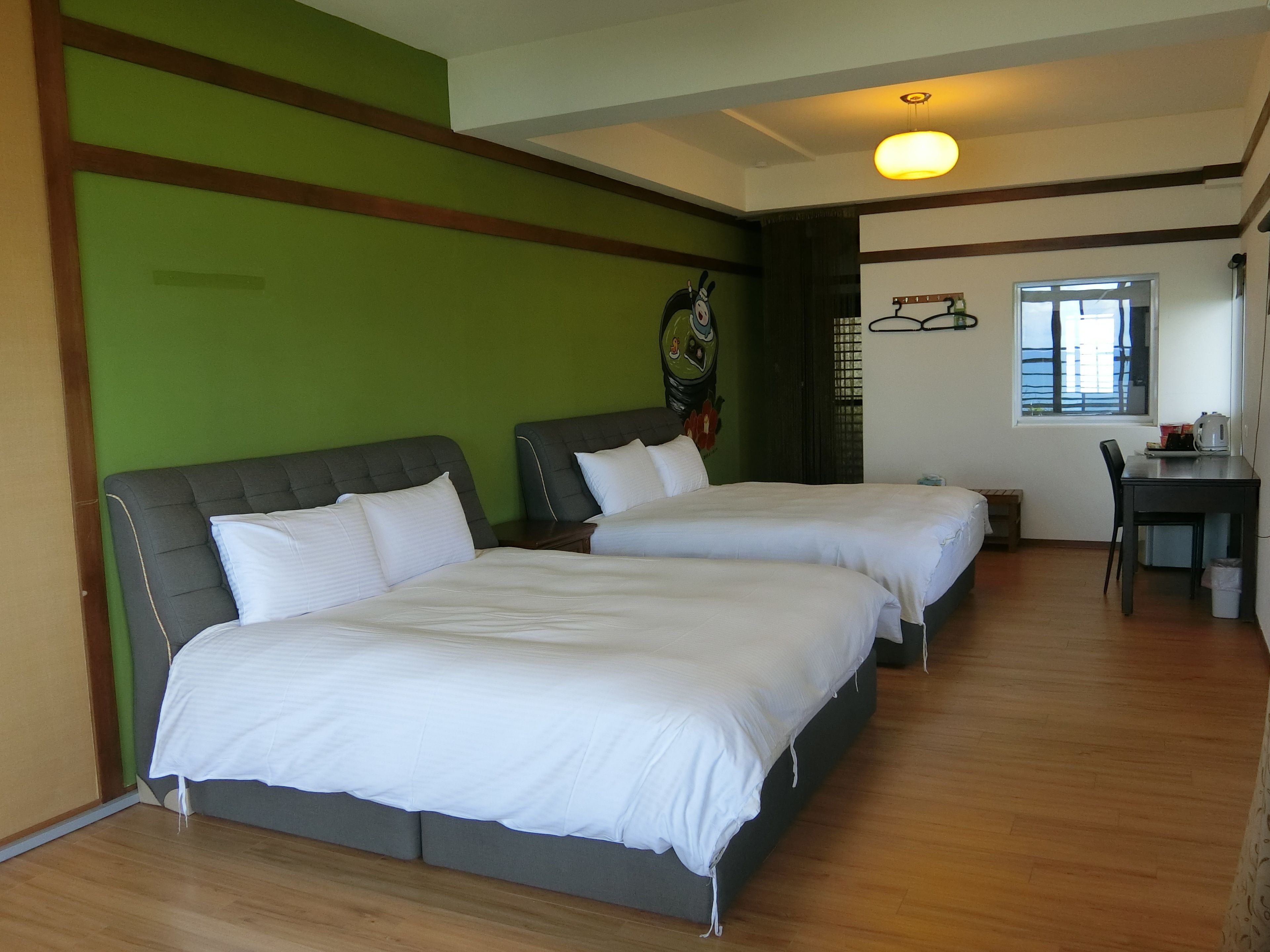 A hotel room with two beds, a desk, and a window.