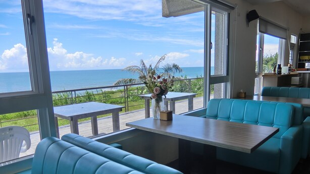 Un restaurante con asientos color turquesa, ventanas amplias y vista al océano.