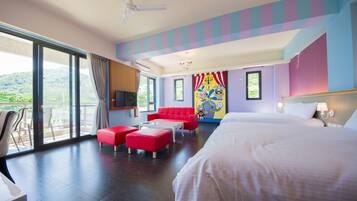 Habitación de hotel con una cama grande, un sofá rojo, una mesa de centro y un balcón con vistas a zonas verdes.
