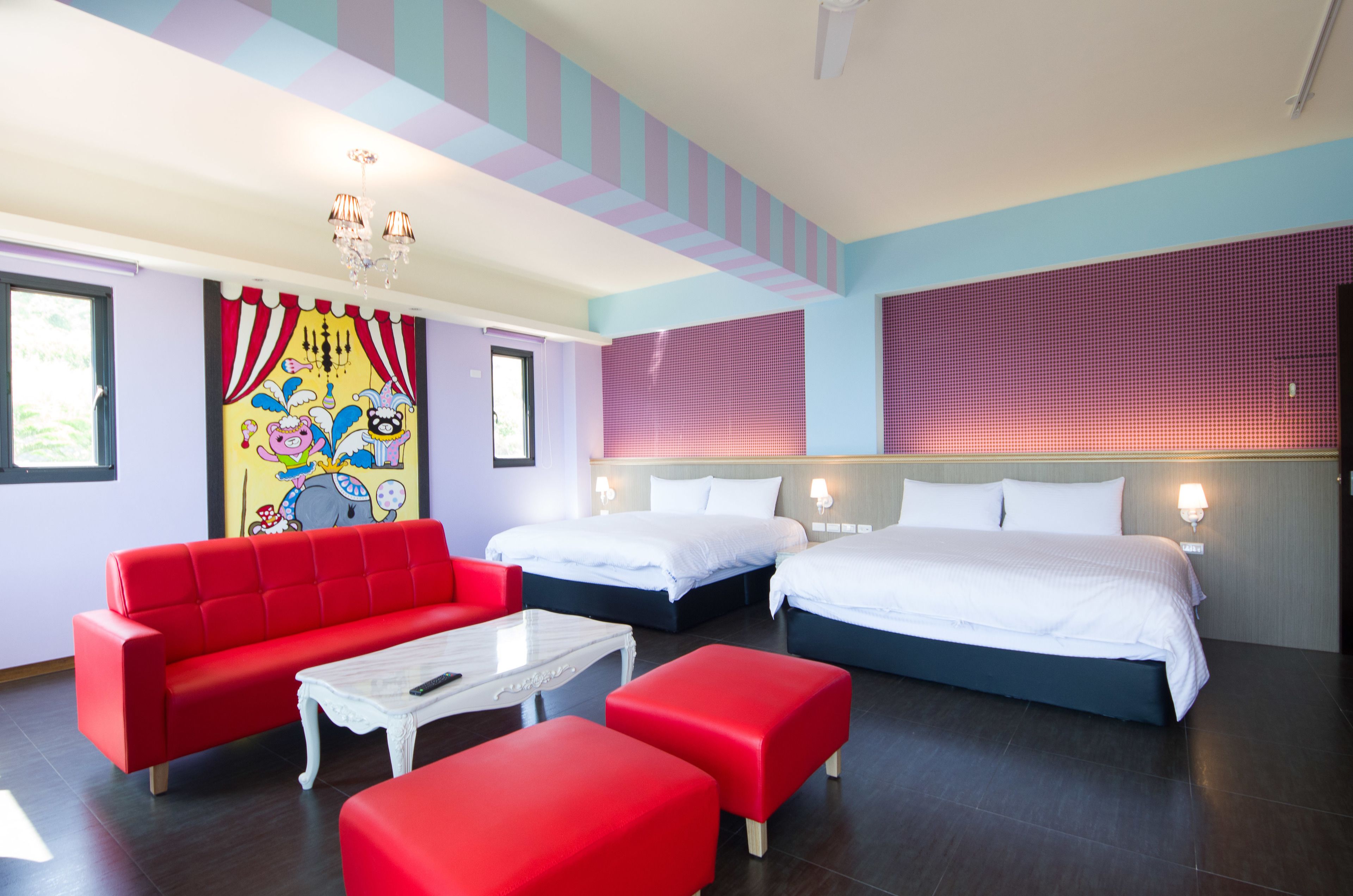 Una habitación de hotel con dos camas, un sofá rojo, una mesita de café blanca y un mural colorido en la pared.