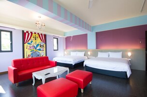 Una habitación de hotel con dos camas, un sofá rojo, una mesita de café blanca y un mural colorido en la pared.
