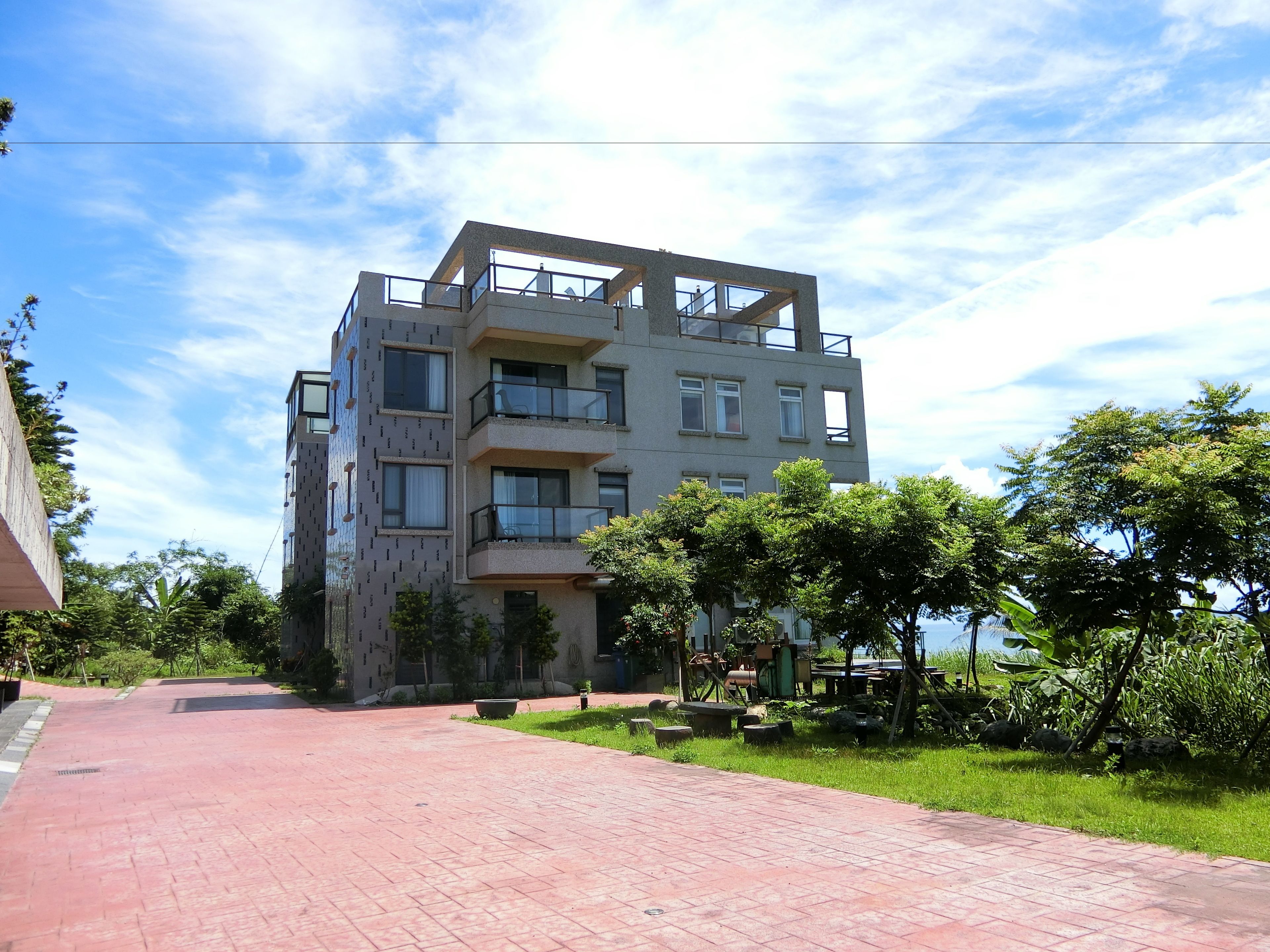 A multi-story building with balconies, a paved walkway, and surrounding greenery.