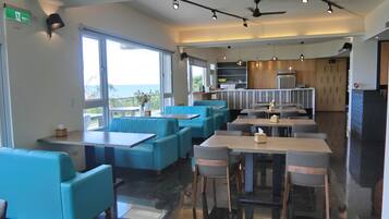 A modern restaurant with blue seating, a kitchen area, and large windows offering a view.