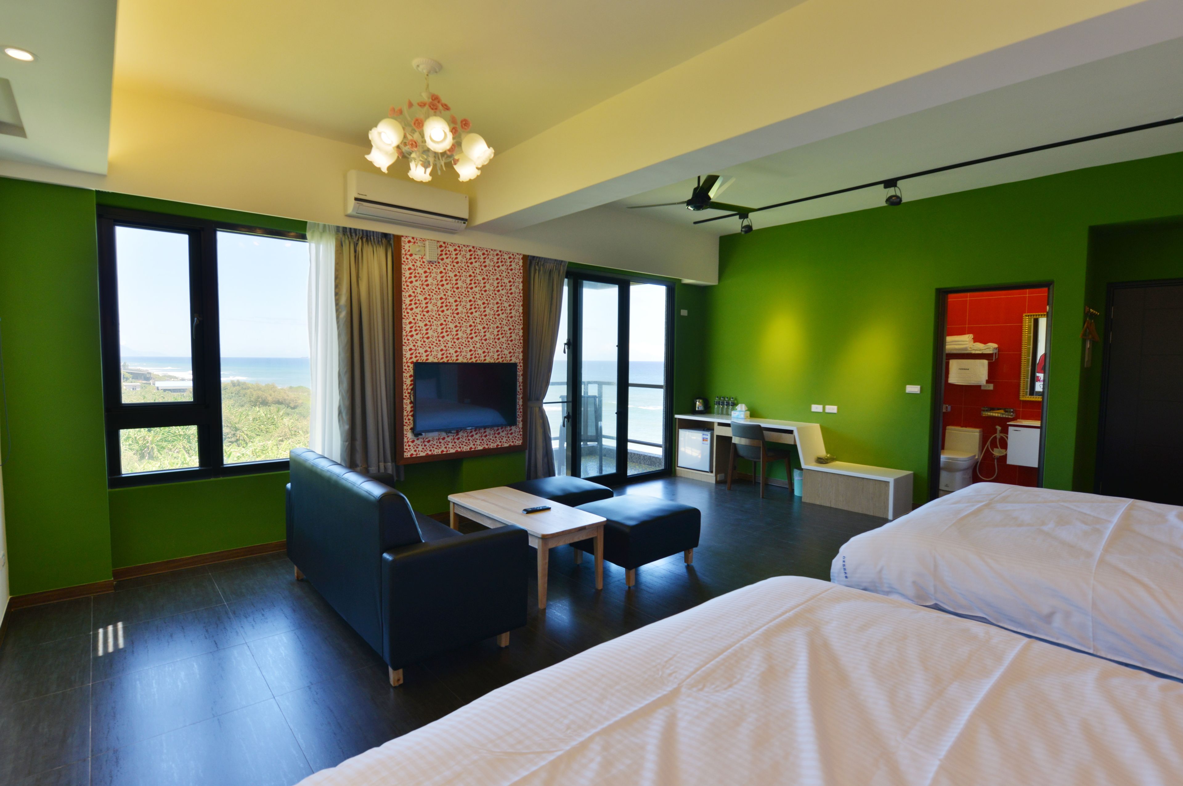 Quarto de hotel com duas camas, televisão, escrivaninha e vista para o mar.