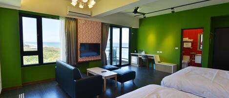Quarto de hotel com duas camas, televisão, escrivaninha e vista para o mar.