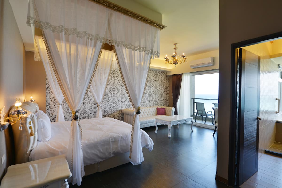 Una cama con dosel con sábanas blancas, un chaise lounge, una mesita y un candelabro.