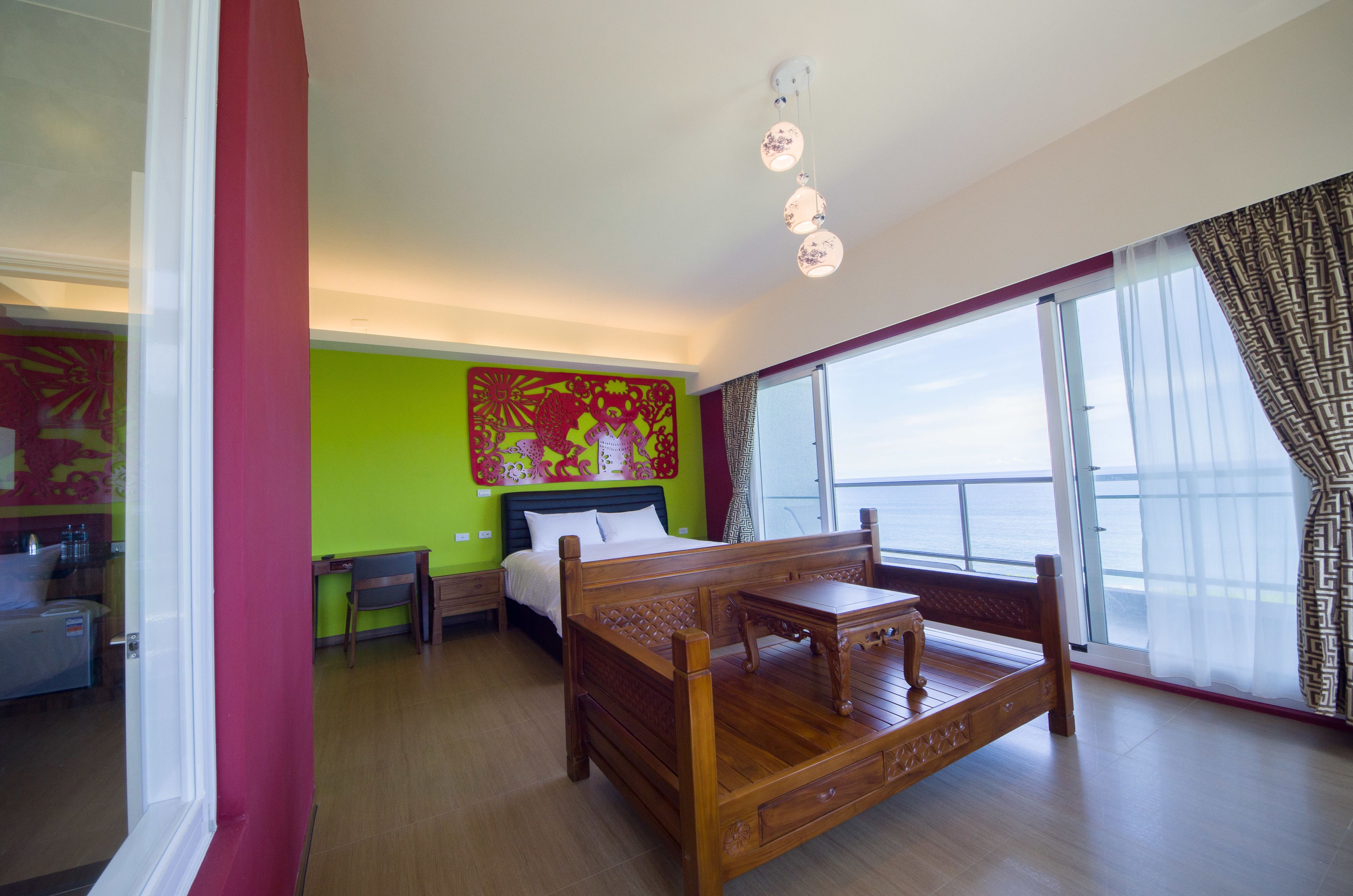 A hotel room with a wooden bed, a desk, a chair, a large window with a view, and a green accent wall.