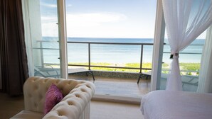 Un dormitorio con un amplio ventanal con vistas al mar, una cama, un sillón con cojines y un balcón con barandilla de cristal.