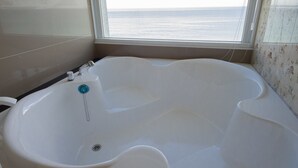 Un baño con una bañera grande, una ventana con vistas al mar y paredes con azulejos.