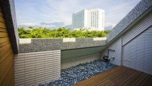 Terraço moderno no telhado, com parede de pedra, deck de madeira e vista para um edifício alto e vegetação.