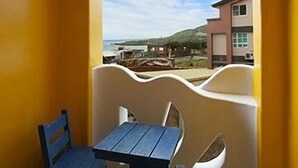 A room with a yellow wall, a window with a view of a beach and buildings, a table, and two chairs. - Dragon Resort of Hotel (Hengchun)