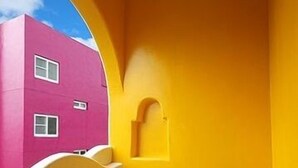 A room with a yellow wall, a pink building outside the window, and a small table with a chair. - Dragon Resort of Hotel (Hengchun)