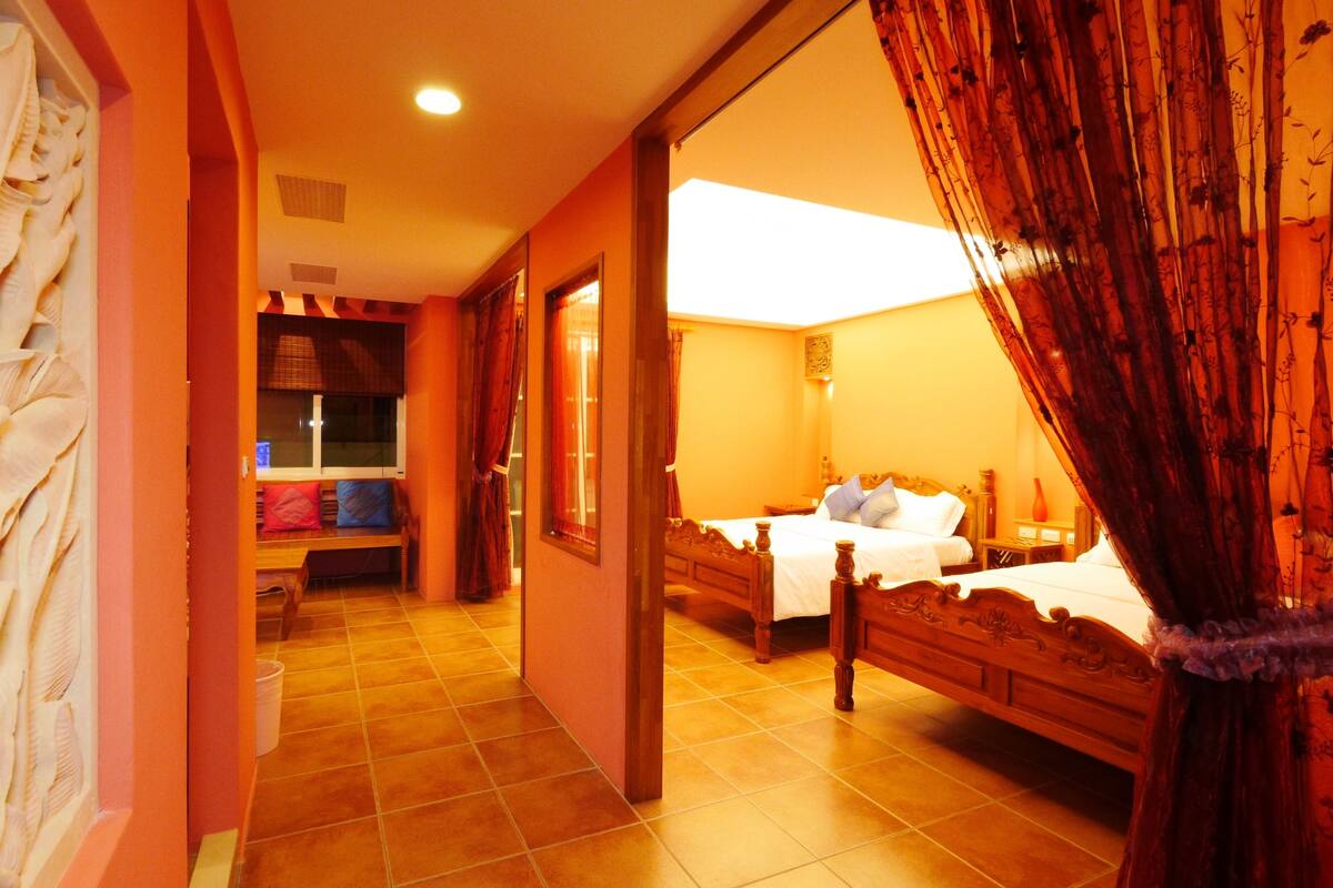 A hotel room with two beds, a sitting area with a bench, and a view of the outside.