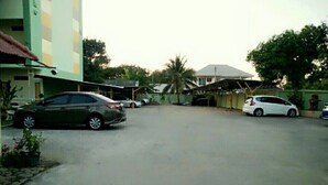 A parking area with two cars, a building with a green facade, and a palm tree in the background. - Lamphun Place (Lamphun)