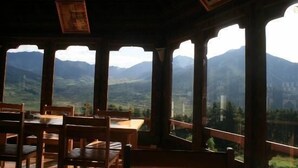 Un comedor con mesa y sillas, ventanas amplias con vistas a la montaña y vigas de madera en el techo.
