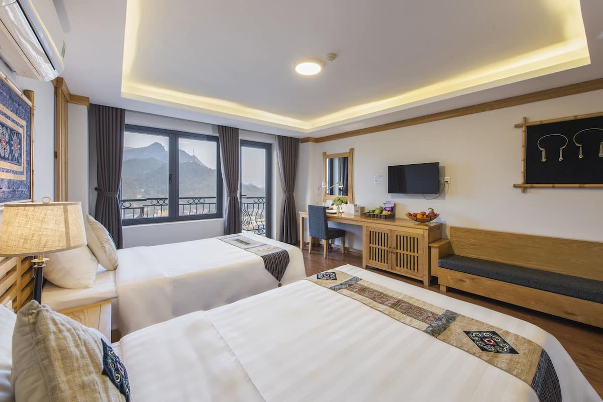 Ein Hotelzimmer mit zwei Betten, einem Schreibtisch, einem Fernseher und einem Balkon mit Bergblick.